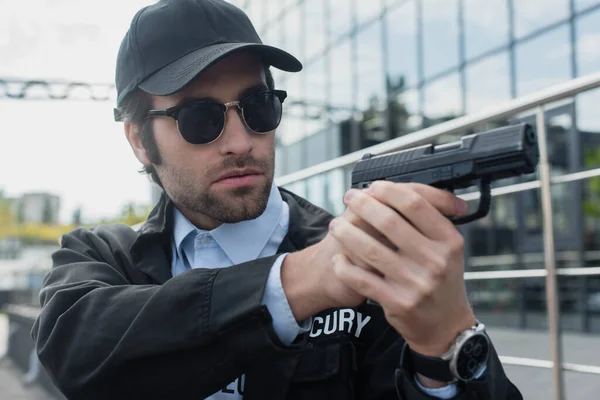 Young guard in uniform and sunglasses holding gun outdoors — Stock Photo