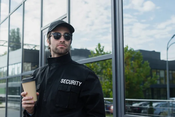 Охоронець в чорній формі і сонцезахисні окуляри, що тримають каву, щоб вийти на вулицю — стокове фото