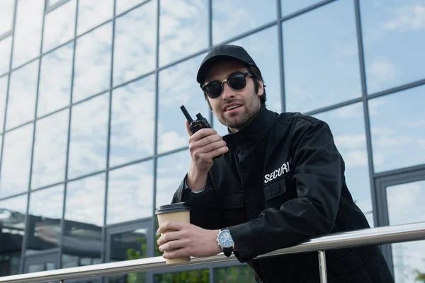 Smiling guard with takeaway drink talking on walkie-talkie outdoors — Stock Photo