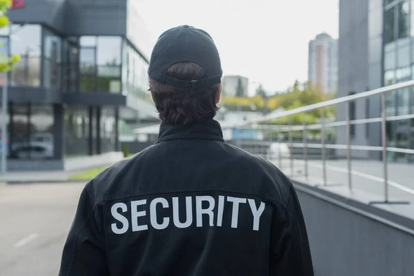 Back view of guard in uniform with security lettering standing on city street — Stock Photo