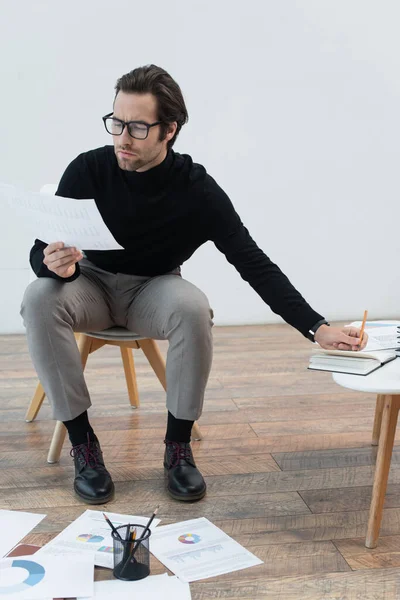 Man in eyeglasses looking at paper while writing in notebook — Stock Photo