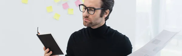Young man in eyeglasses and black turtleneck working with notebook and document, banner — Stock Photo