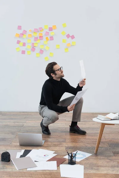 Jeune homme travaillant avec des documents près d'un ordinateur portable et des papiers sur le sol — Photo de stock