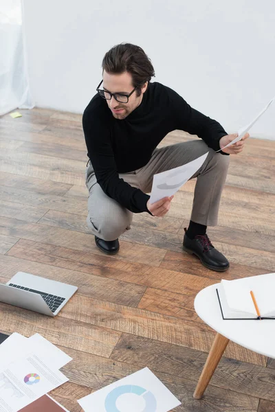 Stilvoller Mann schaut auf Laptop auf dem Boden, während er mit Dokumenten arbeitet — Stockfoto