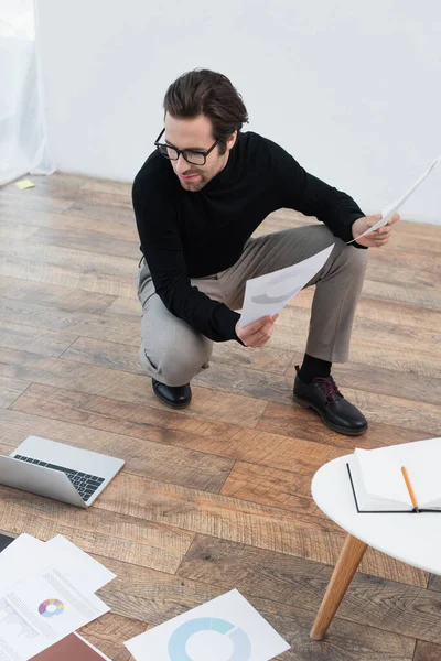 Homem elegante olhando para laptop no chão enquanto trabalhava com documentos — Fotografia de Stock