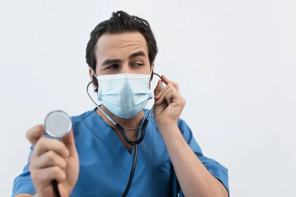 Médico pensativo em máscara médica usando estetoscópio isolado em cinza — Fotografia de Stock