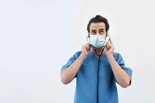 Médico pensativo em máscara médica usando estetoscópio isolado em cinza — Fotografia de Stock