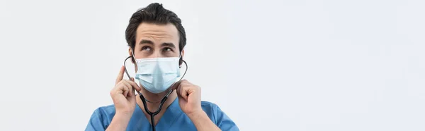 Medico premuroso in maschera medica utilizzando stetoscopio isolato su grigio, banner — Foto stock