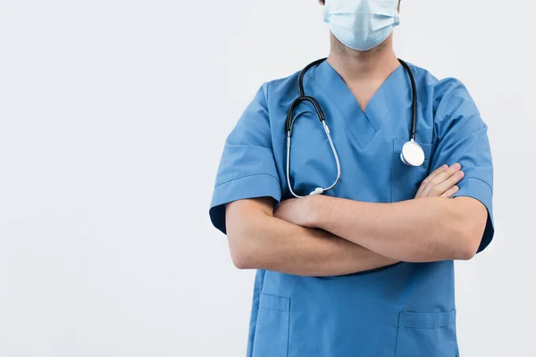 Vista ritagliata del medico in uniforme blu e maschera medica in piedi con braccia incrociate isolate su grigio — Foto stock