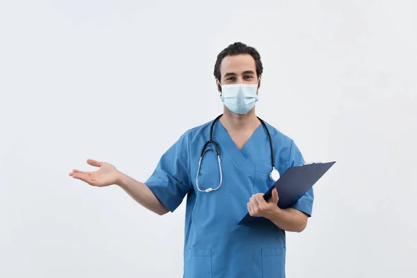 Врач в медицинской маске держит планшет и указывает рукой, изолированной на сером — стоковое фото