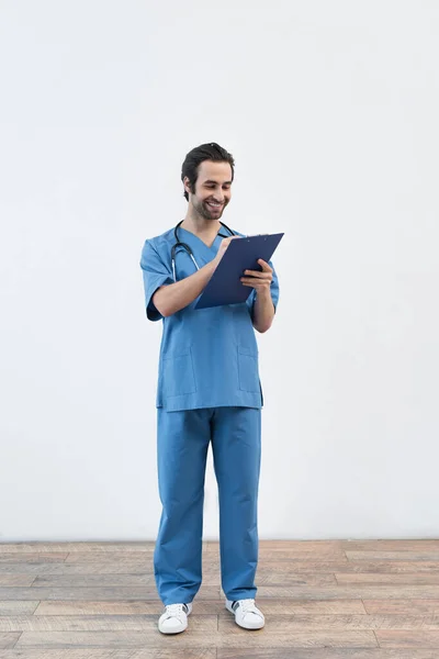 Full length view of happy doctor writing on clipboard near grey wall — Stock Photo