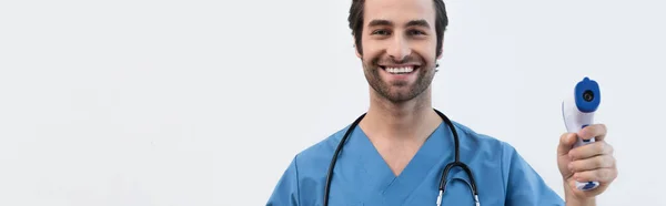 Glücklicher junger Arzt mit Pyrometer, Kamera isoliert auf grauem Banner — Stockfoto