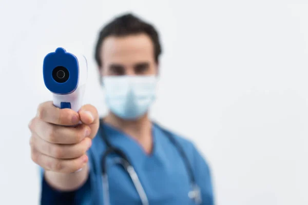 Розмитий лікар в медичній масці тримає пірометр ізольовано на сірому — стокове фото