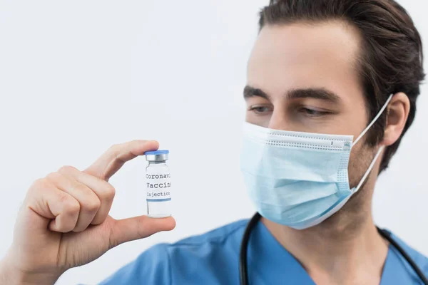 Médecin flou dans un masque médical tenant le vaccin contre le coronavirus isolé sur gris — Photo de stock