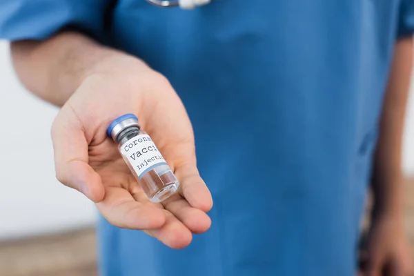 Обрізаний вид розмитого лікаря, що тримає флакон з вакциною проти коронавірусу — стокове фото