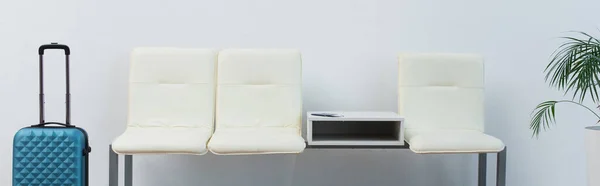 Sièges blancs et valise turquoise dans le salon de départ, bannière — Photo de stock