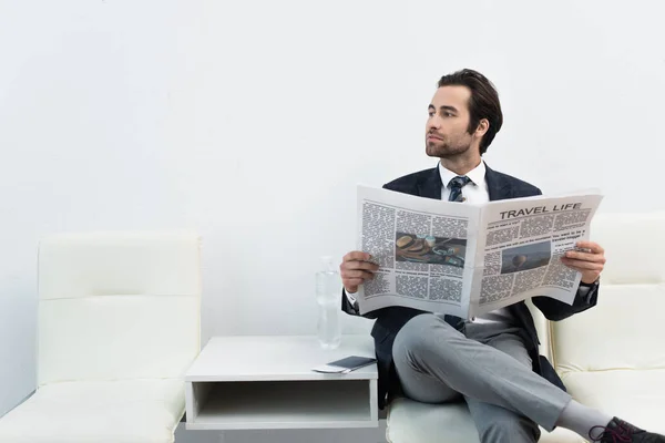Hombre con vida de viaje periódico mirando hacia otro lado mientras está sentado en la sala de salida - foto de stock