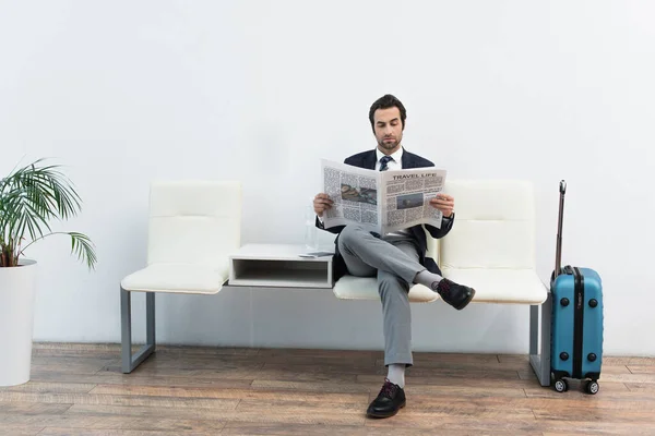 Uomo che legge il giornale nella sala partenze vicino alla valigia — Foto stock