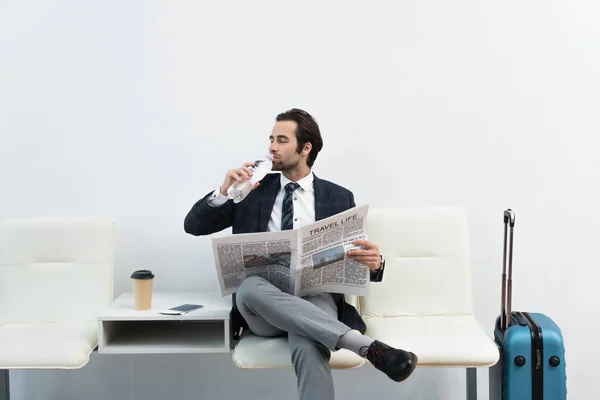 Hombre beber agua mientras está sentado en la sala de salida con la vida de viaje periódico - foto de stock