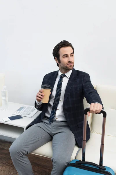 Uomo con drink da asporto che distoglie lo sguardo mentre aspetta nella sala partenze — Foto stock
