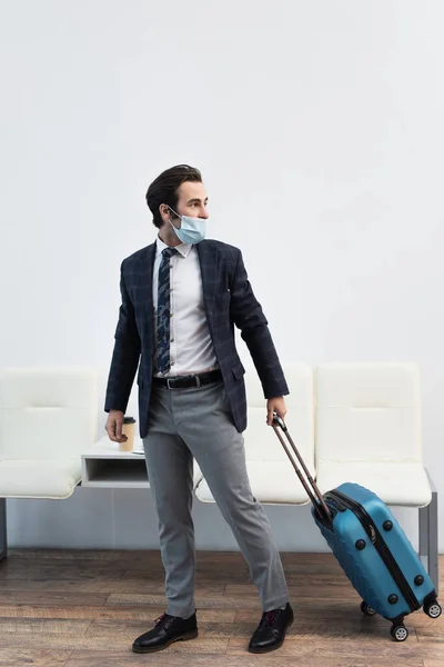 Hombre con máscara médica mirando hacia otro lado mientras lleva la bolsa de viaje en la sala de salida - foto de stock