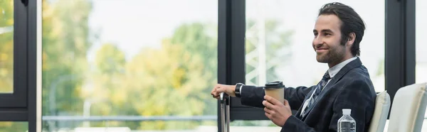 Hombre feliz con bebida para llevar esperando en la sala de salida, pancarta - foto de stock