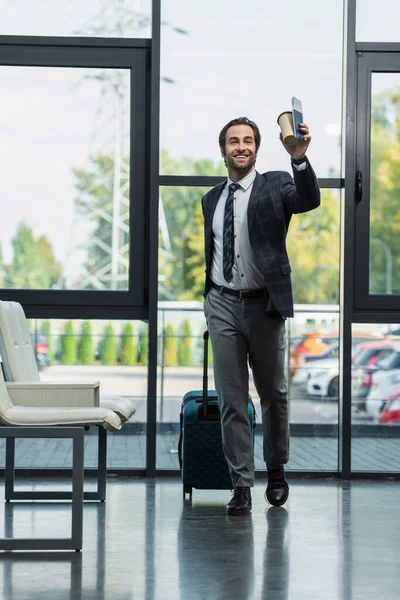 Glücklicher Mann mit Koffer, Pappbecher und Reisepass, der beim Gang in die Abflughalle wegschaut — Stockfoto