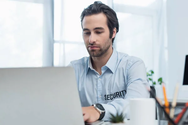 Sicherheitsmann tippt im Überwachungsraum auf verschwommenem Laptop — Stockfoto