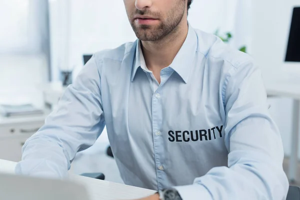 Vista recortada del hombre de seguridad que trabaja en la computadora portátil borrosa en la oficina - foto de stock