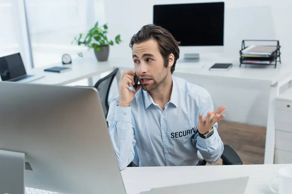 Hombre de seguridad haciendo gestos mientras habla por teléfono móvil en la sala de supervisión - foto de stock