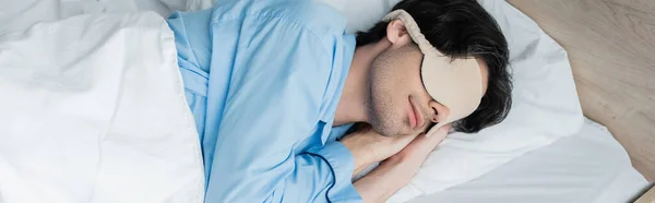 Joven durmiendo en ropa de cama blanca en pijama azul y máscara para dormir, pancarta - foto de stock