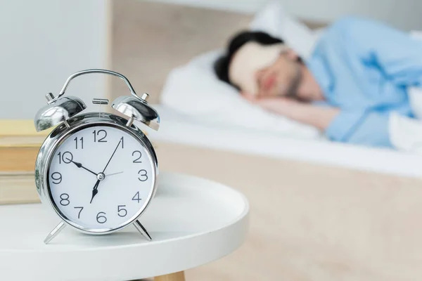 Selective focus of vintage alarm clock near man sleeping on blurred background — Stock Photo