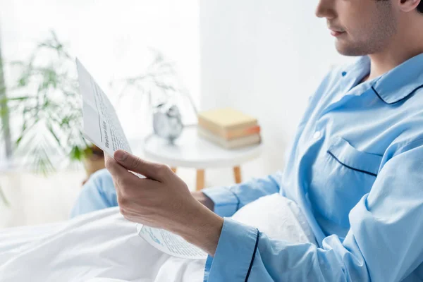 Vista ritagliata dell'uomo in pigiama blu che legge il giornale del mattino a letto — Foto stock