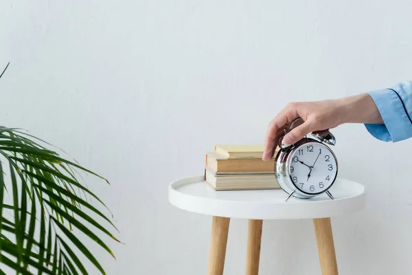 Partial view of man turning off vintage alarm clock on bedside table near books — Stock Photo