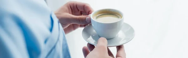 Vue recadrée de l'homme en pyjama tenant soucoupe avec tasse de café, bannière — Photo de stock