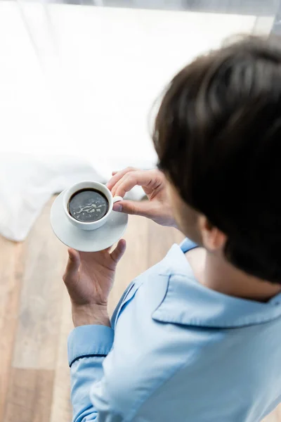 Vista aérea del hombre borroso en pijama sosteniendo una taza de café - foto de stock