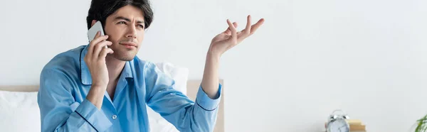 Thoughtful man gesturing while talking on mobile phone in bedroom, banner — Stock Photo