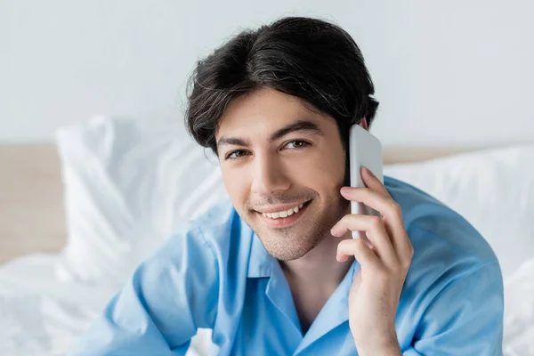 Hombre satisfecho mirando a la cámara mientras habla en el teléfono móvil en el dormitorio - foto de stock