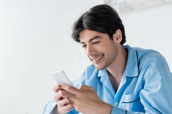 Homem morena feliz em pijama azul conversando no telefone móvel — Fotografia de Stock