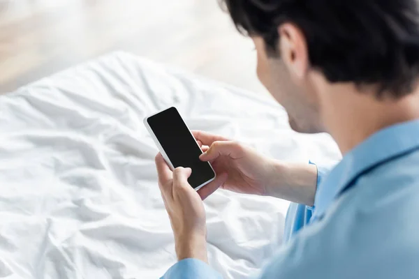 Hombre borroso sosteniendo el teléfono móvil con pantalla en blanco en el dormitorio - foto de stock