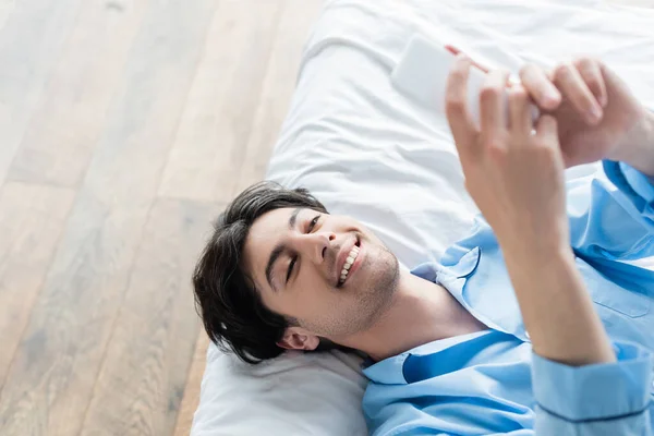 Overhead-Ansicht des glücklichen Mannes auf dem Bett liegend und Nachrichten auf dem Handy — Stockfoto