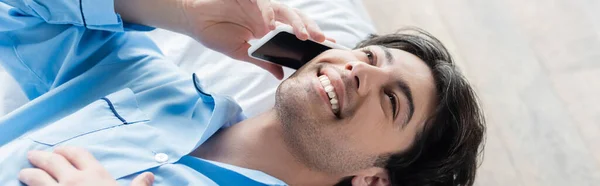 Vue aérienne de jeune homme heureux parlant sur smartphone au lit, bannière — Photo de stock