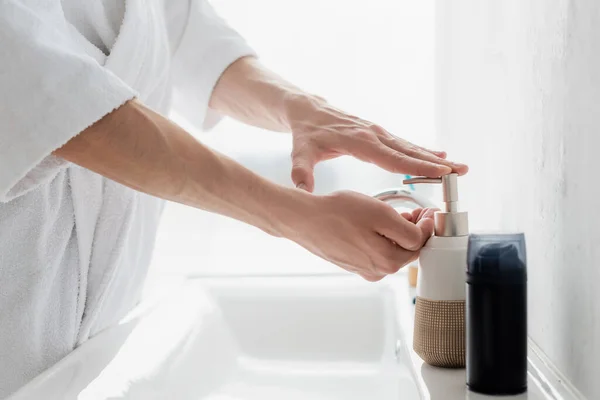 Cropped view of man in bathrobe applying liquid soap on hands — Stock Photo