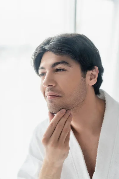 Young brunette man smiling while touching face in bathroom — Stock Photo