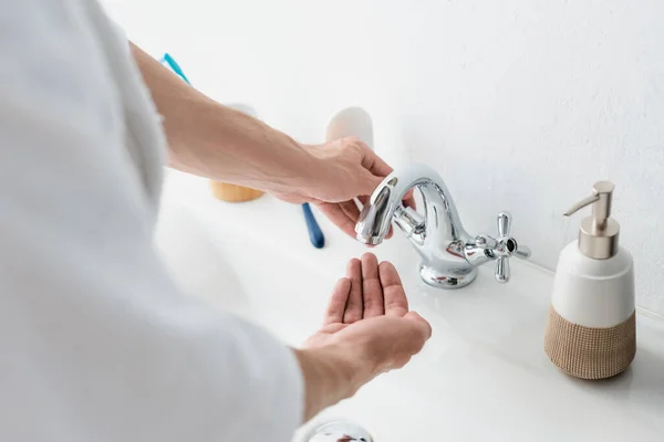 Vue partielle du robinet d'ouverture d'homme flou dans la salle de bain — Photo de stock