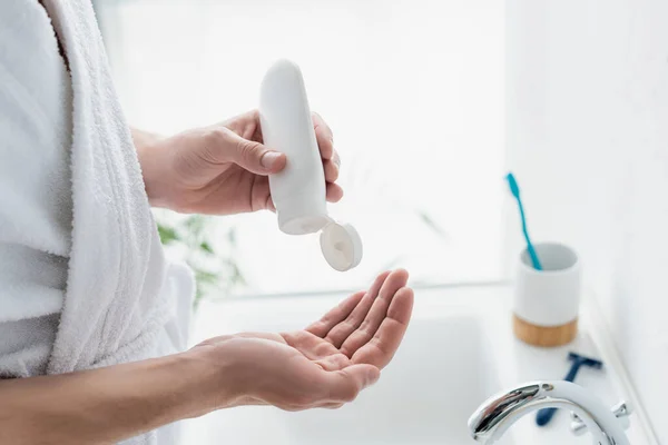 Abgeschnittene Ansicht eines Mannes im weißen Bademantel, der Handcreme in der Nähe des Waschbeckens im Badezimmer aufträgt — Stockfoto