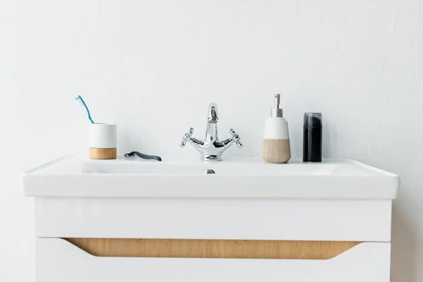 White sink with faucet, dispenser with liquid soap, shaving foam, safety razor and toothbrush — Stock Photo