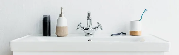 Toothbrush, safety razor, liquid soap and shaving foam on white sink with faucet, banner — Stock Photo