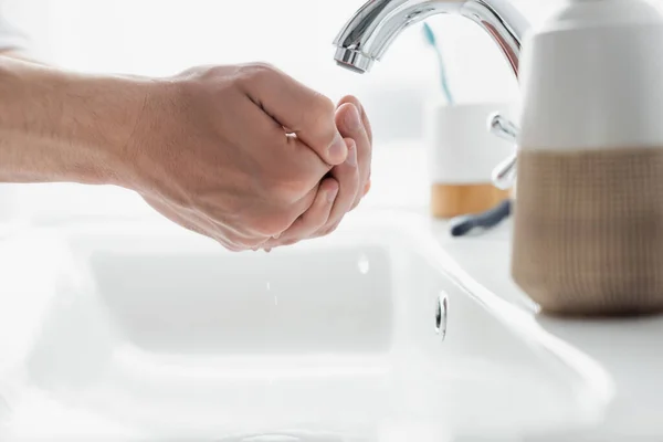 Close up view of male hands near faucet and blurred toiletries — Stock Photo