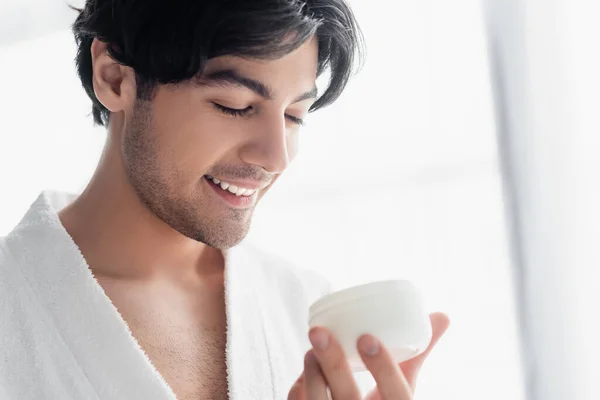 Hombre satisfecho sosteniendo contenedor con crema cosmética en el baño - foto de stock